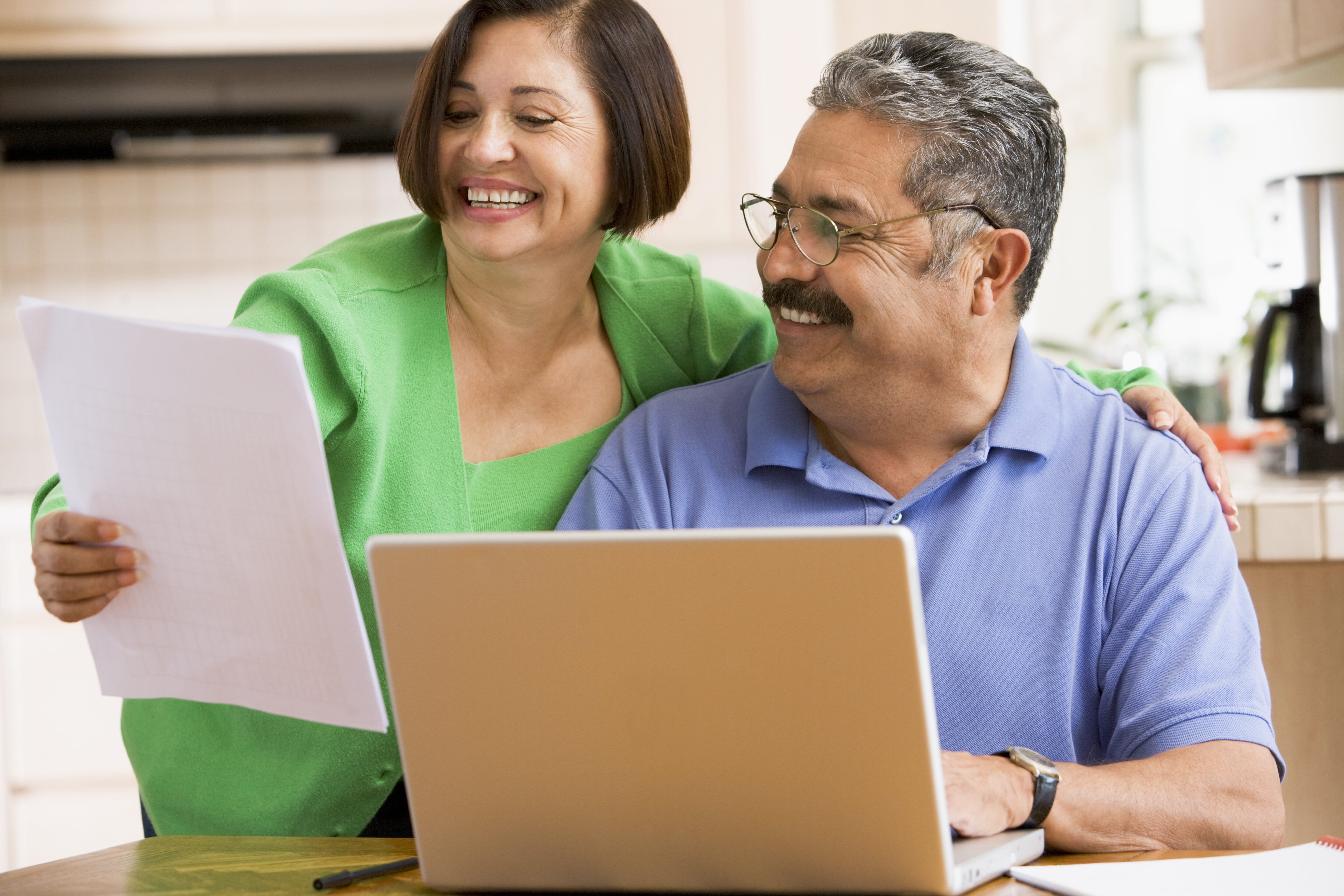 couple-in-kitchen-with-laptop-and-paperwork-smiling